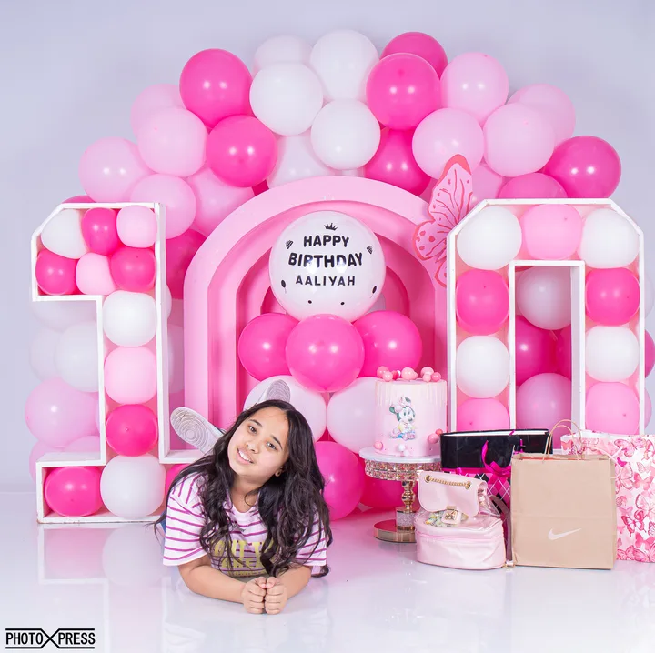 Birthday photoshoot, older girl lying down with gifts and a pink balloon arch