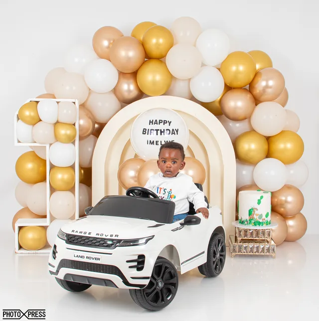 First birthday photoshoot, boy in a toy car with a gold balloon arch