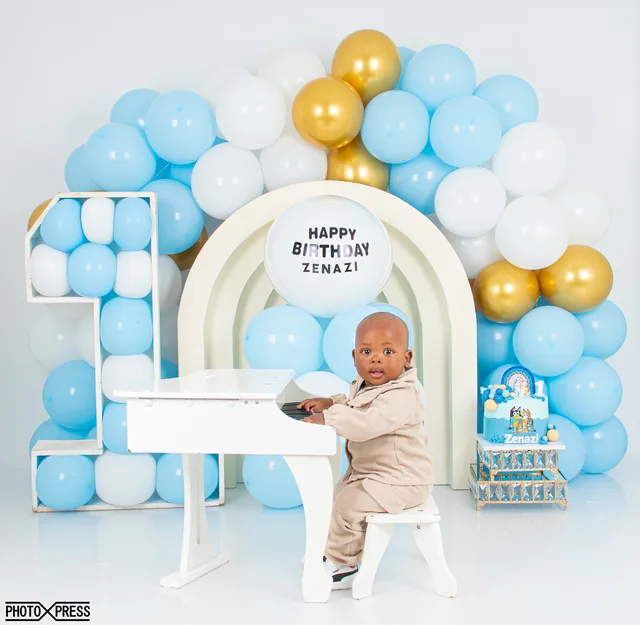 First birthday photoshoot at a toy piano, blue and gold balloon arch