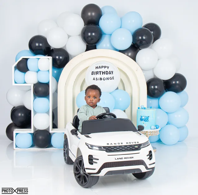 First birthday photoshoot, boy in a toy car with a blue and black balloon arch