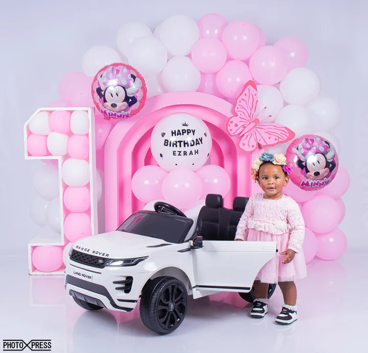 First birthday photoshoot, girl in pink on a toy car, Minnie Mouse themed balloon arch